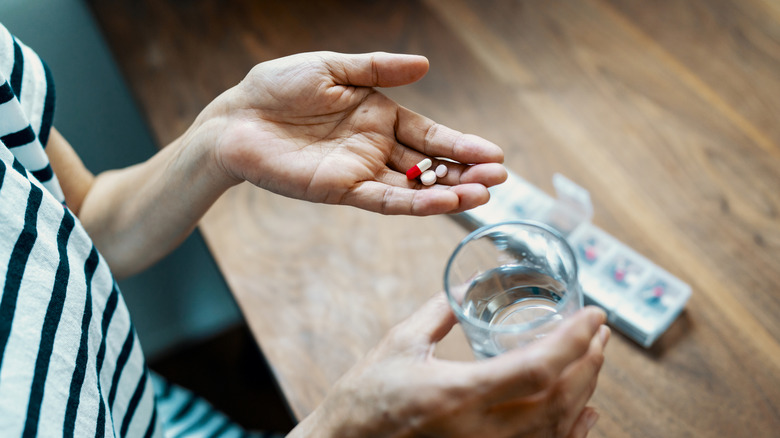 An older woman's hand holding different medication pills