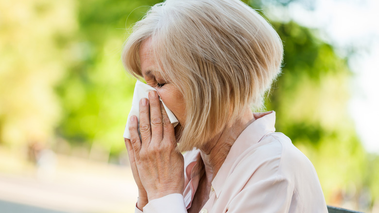 Older woman outside blowing nose