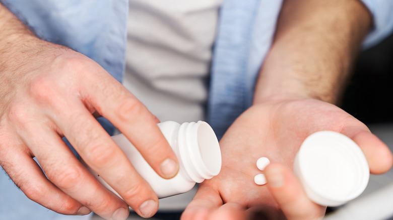 A man's hands holding bottle of aspirin and putting two tablets in his hand