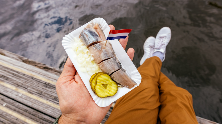 A man holding a small plate of herring with a Netherlands flag toothpick