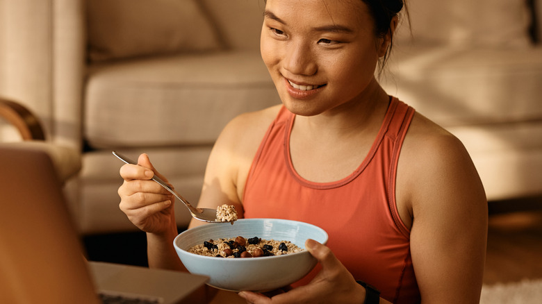A young woman eating a bowl of cereal with dried fruit
