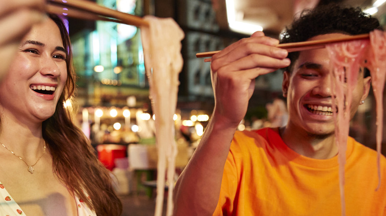 woman and man smiling as they eat noodles