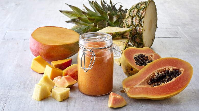 Cut papaya, blended papaya in a jar, and cut pineapple on a gray table