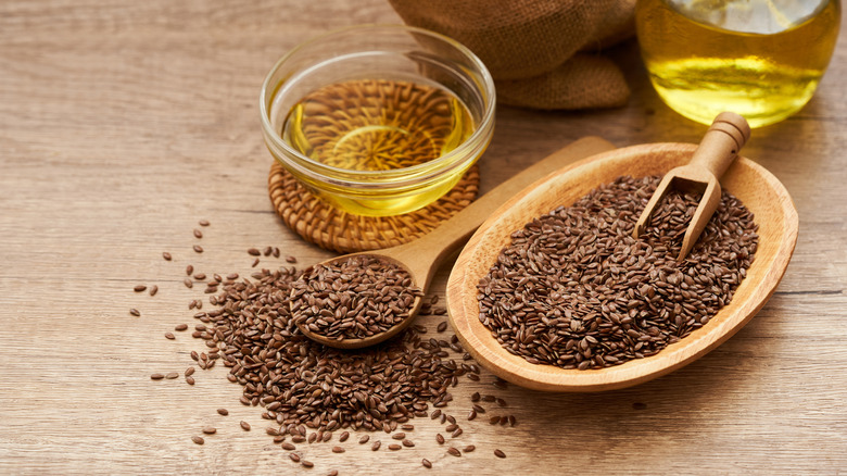 Flaxseeds in a wooden bowl next to small glass bowl of flaxseed oil