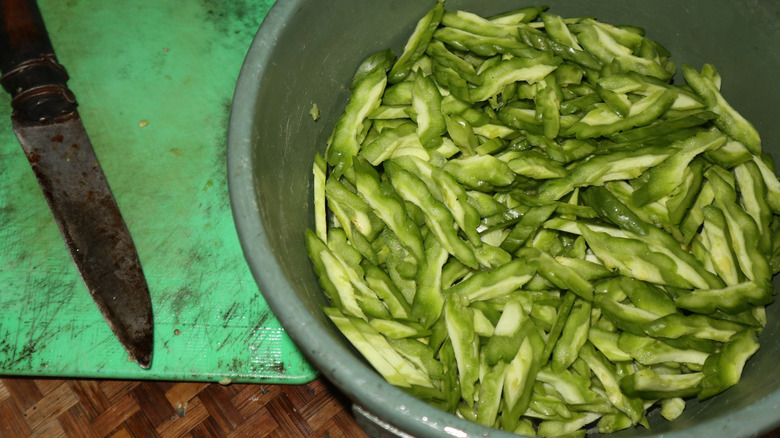 A pan of sliced bitter melon next to a knife and cutting board