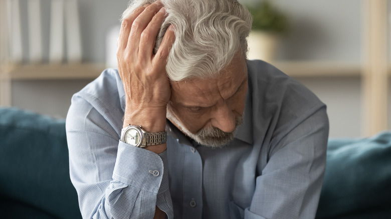 Man sitting leaned over with hand on back of head