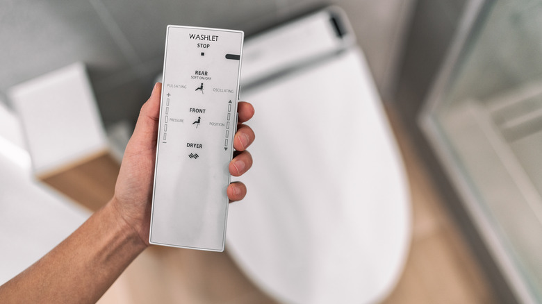 Close up of a hand holding a bidet remote with bidet in background