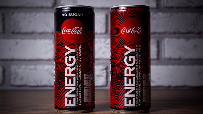 Two cans of Coca-Cola Energy drinks on a table with brick background