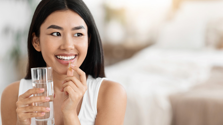 a smiling young woman holds a supplement with a glass of water 