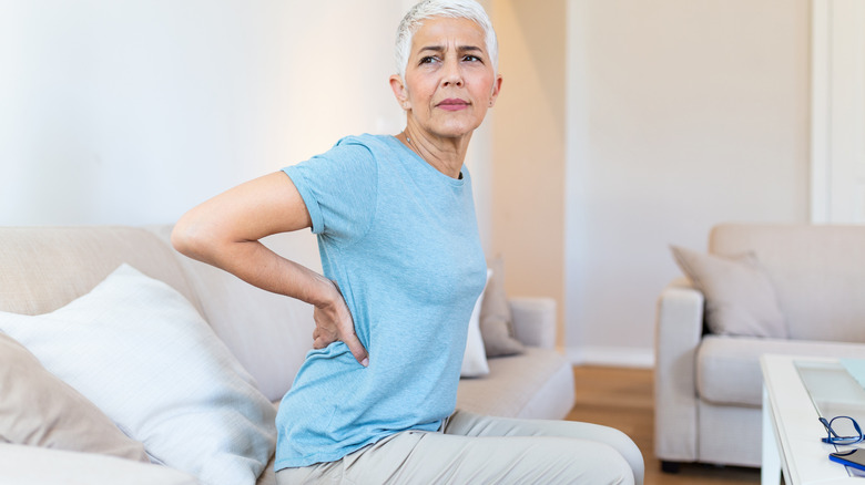 White-haired woman on couch holding lower back