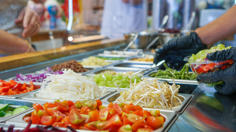 Gloved hand using serving utensils at an open salad bar