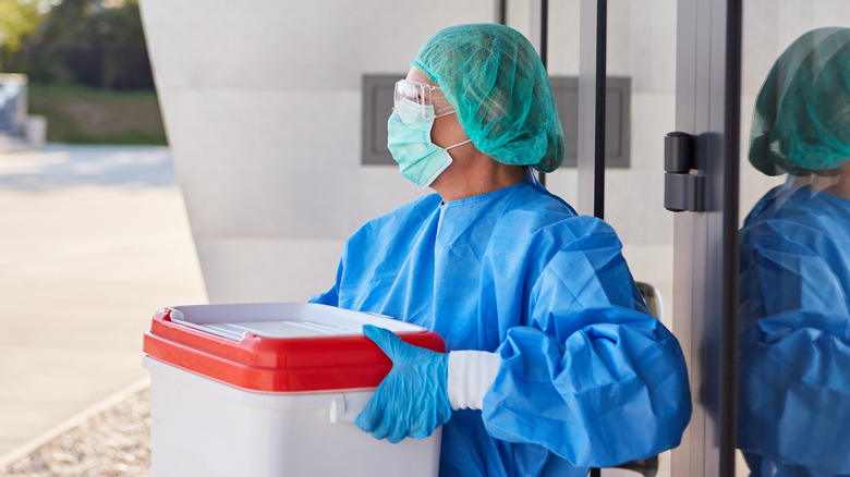 Masked medical professional carrying an organ donation cooler