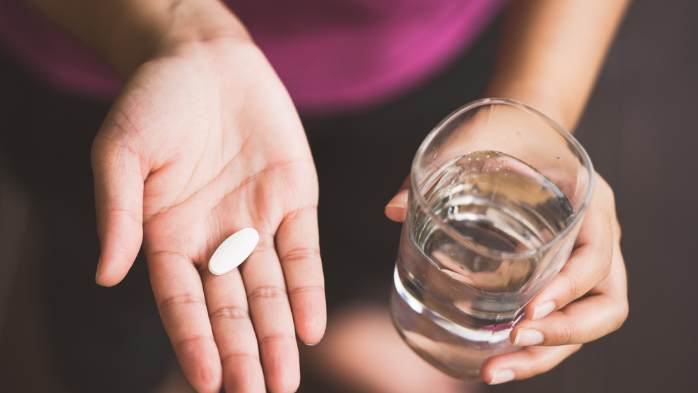 Close up shot of someone holding a pill and glass of water
