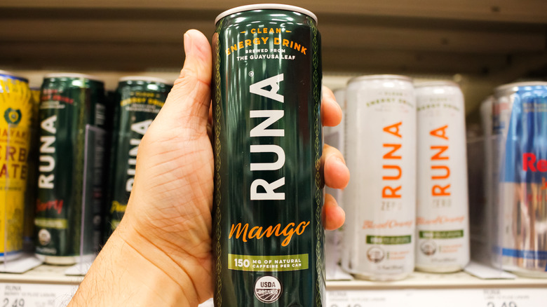 Close up of hand holding a can of Runa energy drink with row of energy drinks on shelf in background