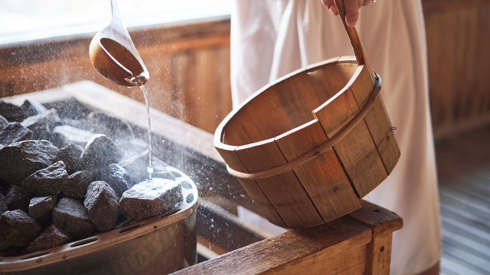 person pouring water over hot rocks in a sauna 