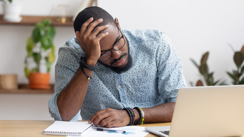 man holding head working at computer