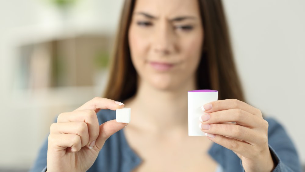 Confused woman doubting between saccharine and sugar at home