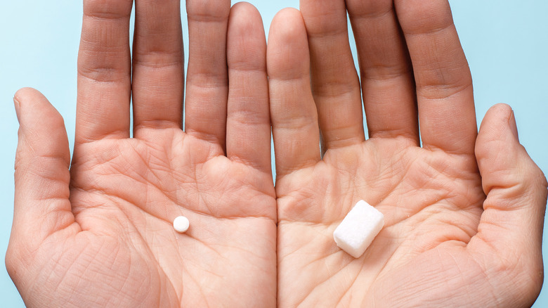 hands holding artificial sweetener and sugar