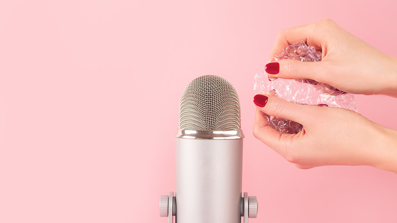 Hands pop bubble wrap near a microphone, against a pink background