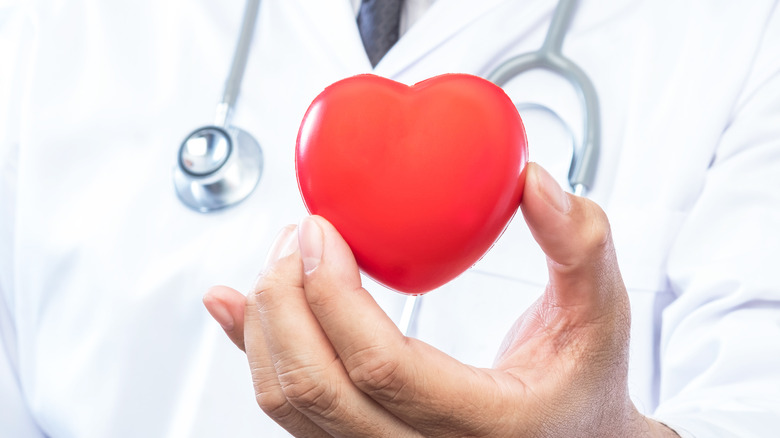 medical doctor wearing a white lab coat holding a red heart in hand
