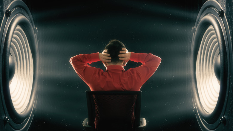 Person sitting between two giant speakers with hands over their ears