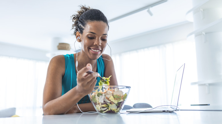 Woman eating salad next to laptop