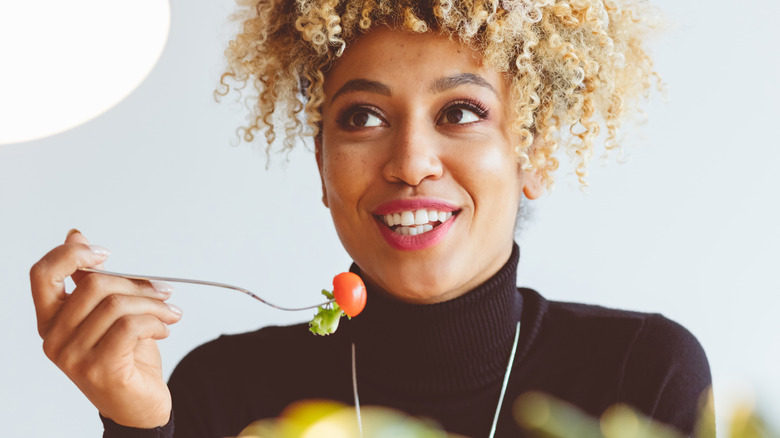 Curly-haired woman eating tomato half