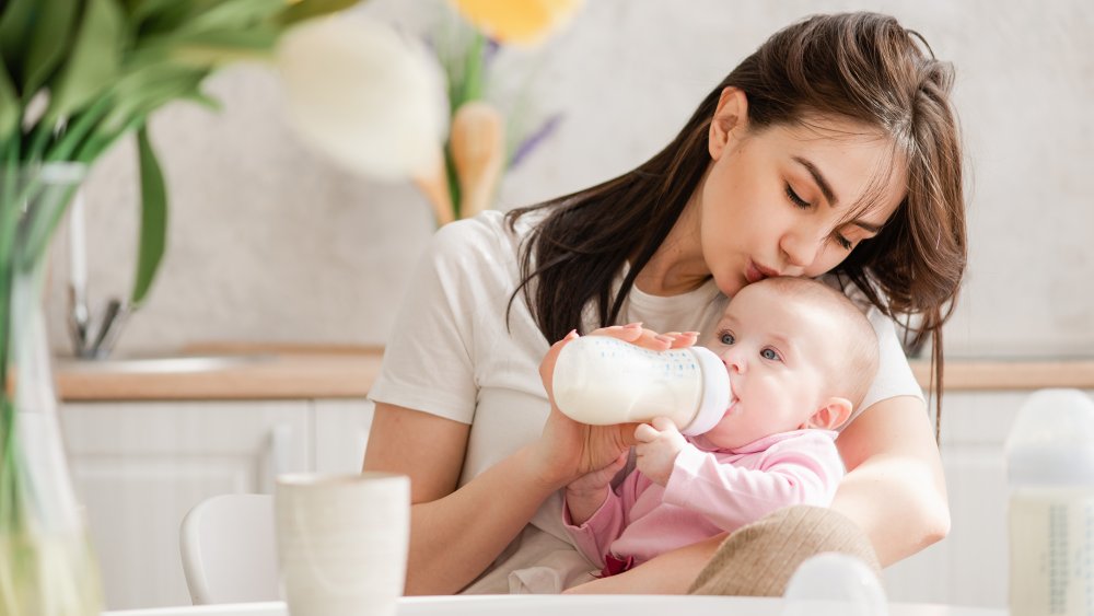 Woman kisses baby drinking from plastic bottle