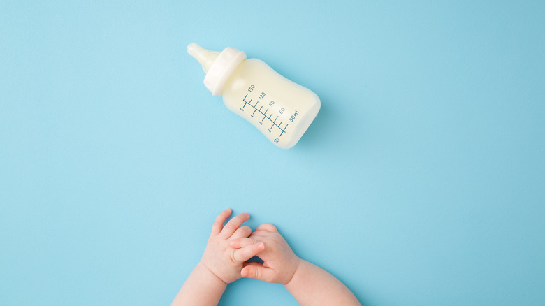 a baby's hands reaching for a bottle of milk 
