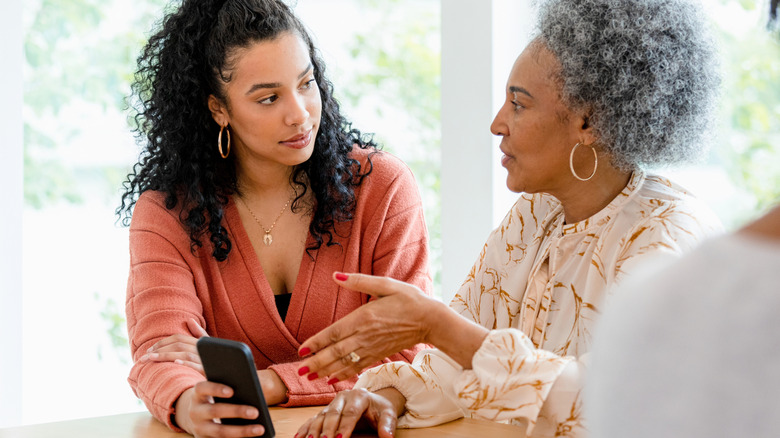 adult daughter speaking with senior mother while holding cell phone