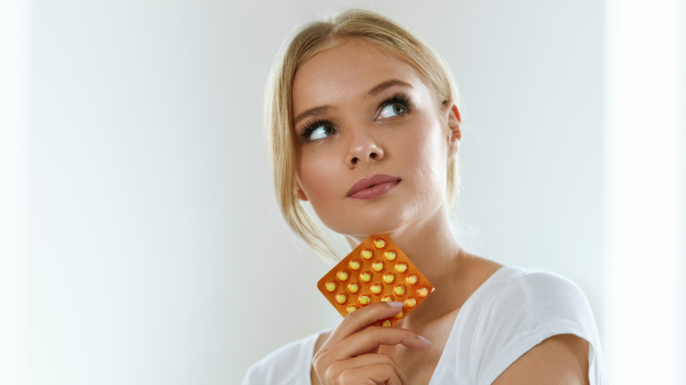 woman holding pack of birth control pills, looking off in the distance