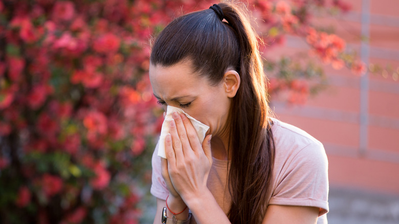 woman sneezing in front of foliage