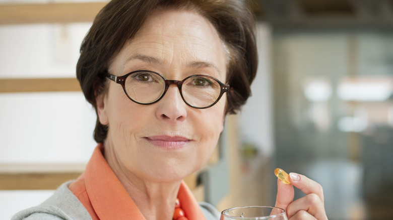 older woman taking a supplement with water