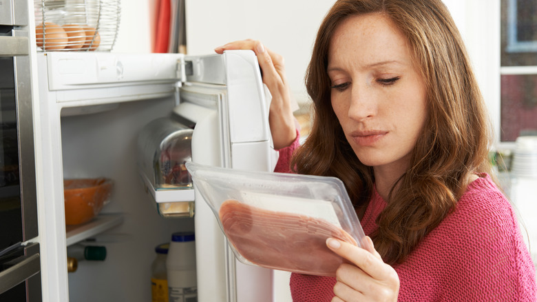 woman peering at packaged meat from fridge