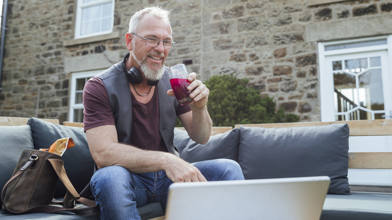 older man drinking dark juice outside while on device