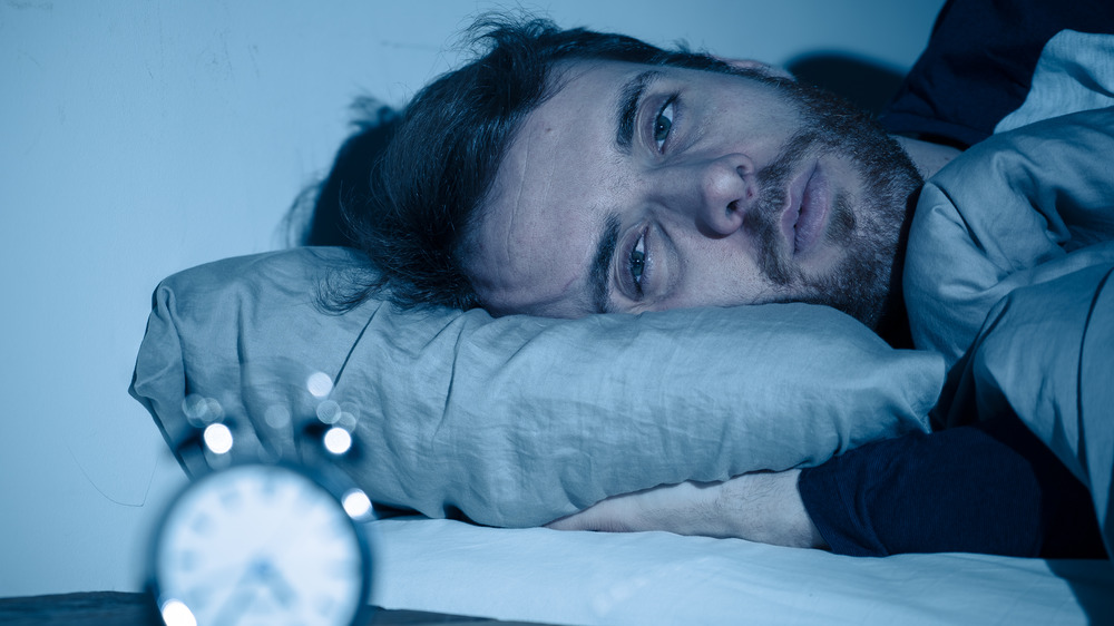 Stock photo of man with insomnia looking at alarm clock