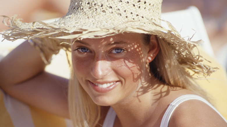 a woman with blond hair and blue eyes wears a sun hat