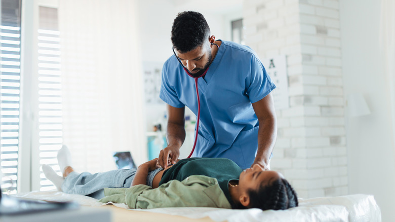 A doctor using a stethoscope to listen to the abdomen of a young girl lying down