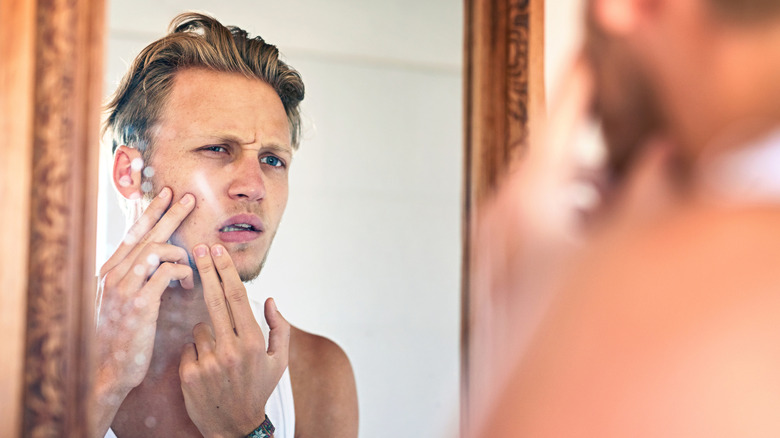 man looking in mirror with unhappy expression due to complexion problems
