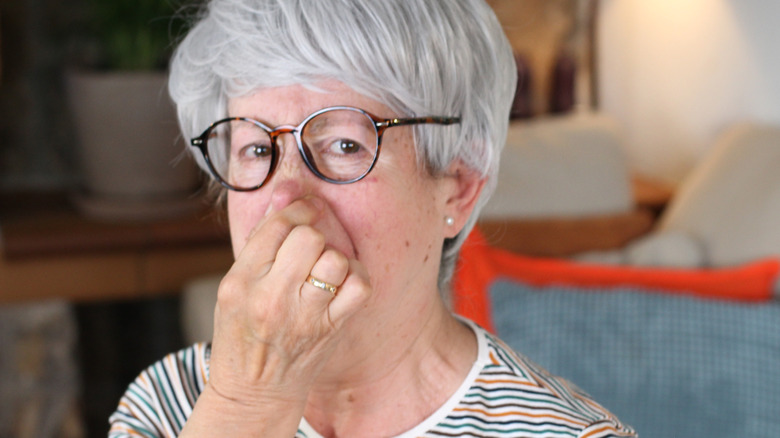 A bespectacled grey-haired woman pinching her nose.