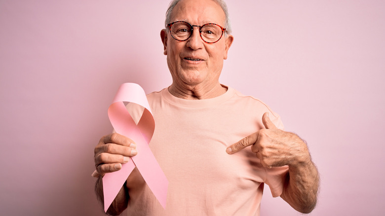 man with breast cancer awareness ribbon and pointing to his breast