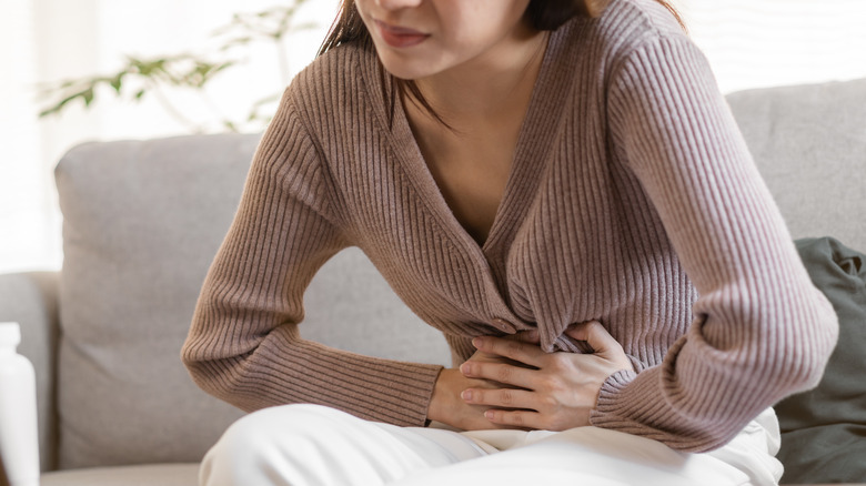 young woman sitting on her couch suffering with cramps