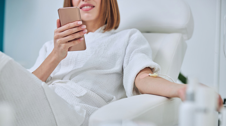 A young woman scrolls her phone while recieving IV 