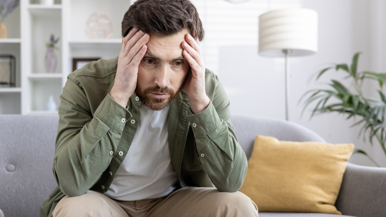 worried man sitting on sofa holding face in hands