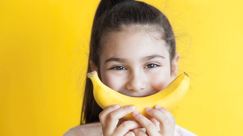 Little girl holding up banana to face