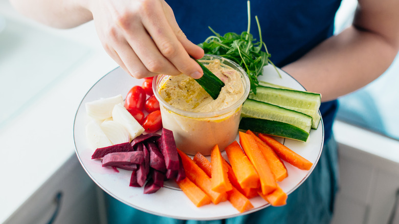 a person with a plant of colorful veggies and hummus