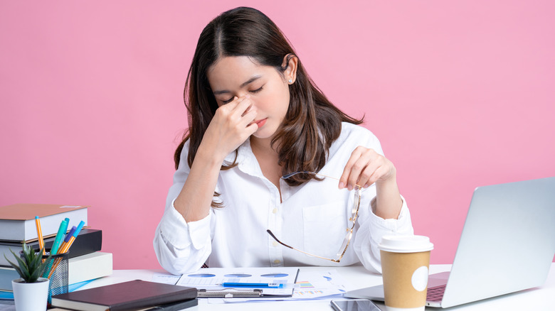 woman rubbing nose at desk