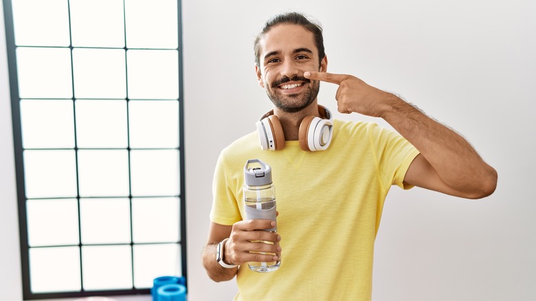 man drinking water and pointing to his face