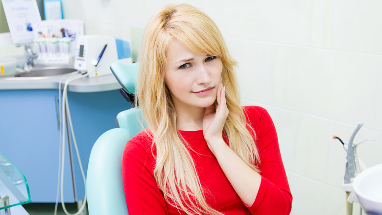 Young girl in dentist chair with hand on her cheek﻿