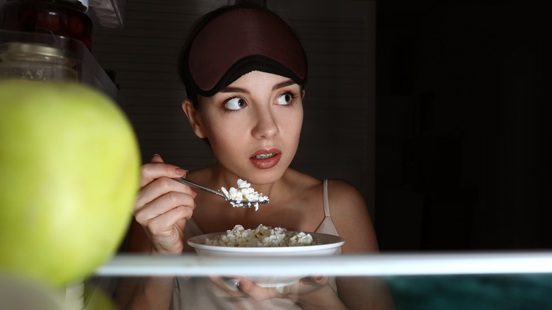 Woman eating cottage cheese straight from the fridge at night 